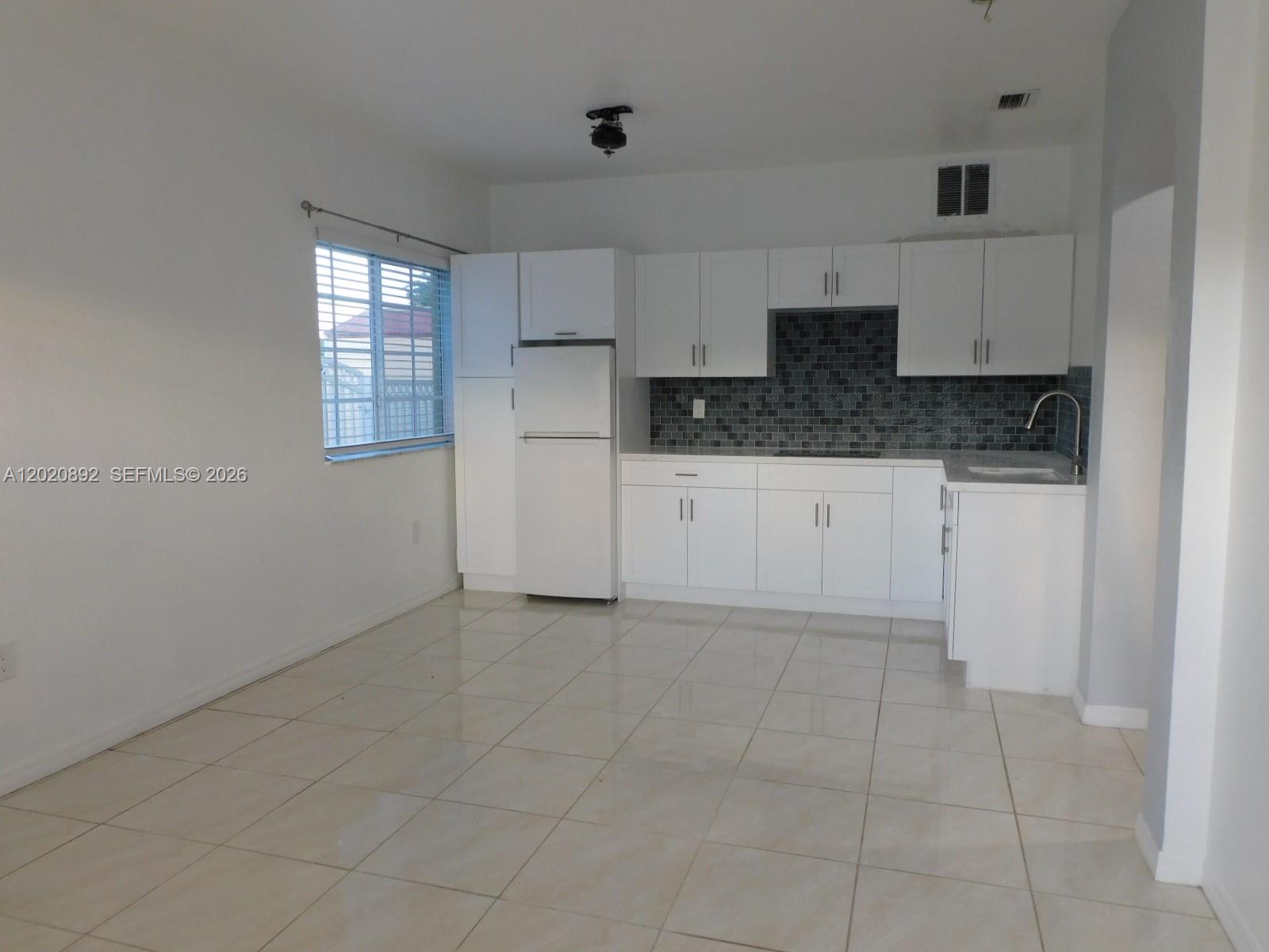 A kitchen features white cabinets, a white refrigerator, and a dark tiled backsplash — 21511 SW 122nd Ct # 0, Miami FL 33177, MIAMI, FL