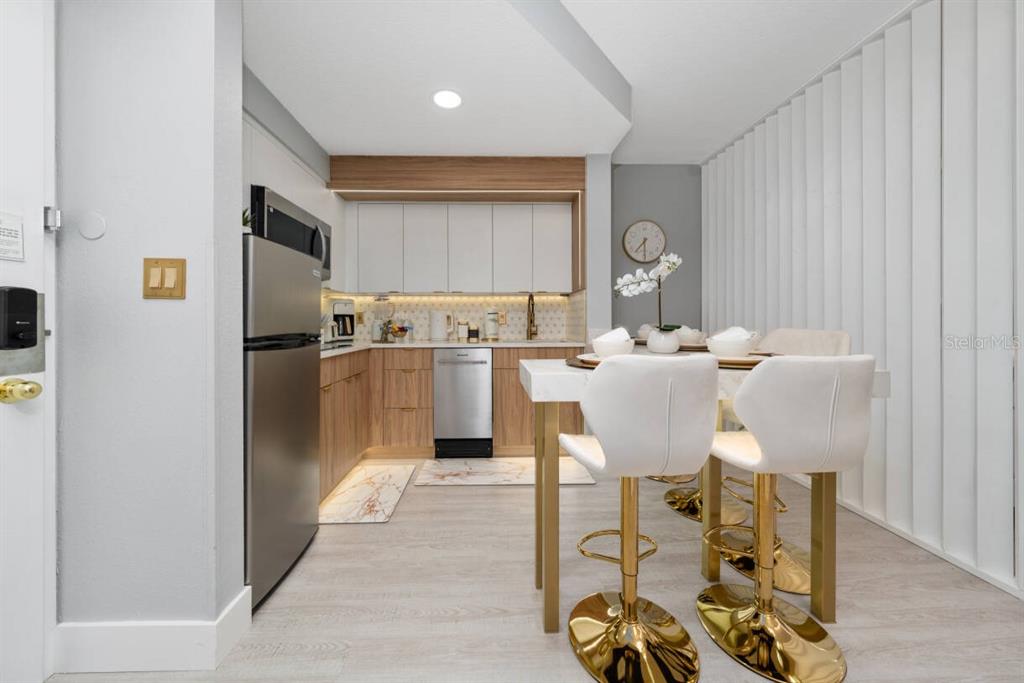 A modern kitchen features light wood cabinets, stainless steel appliances, and a white dining table — 7601 CANADA AVENUE UNIT 614, ORLANDO, FL