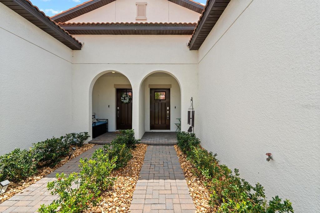 A paved walkway leads to two arched entryways with dark wooden doors on a house — 17538 HOLLY WELL AVENUE, WIMAUMA, FL
