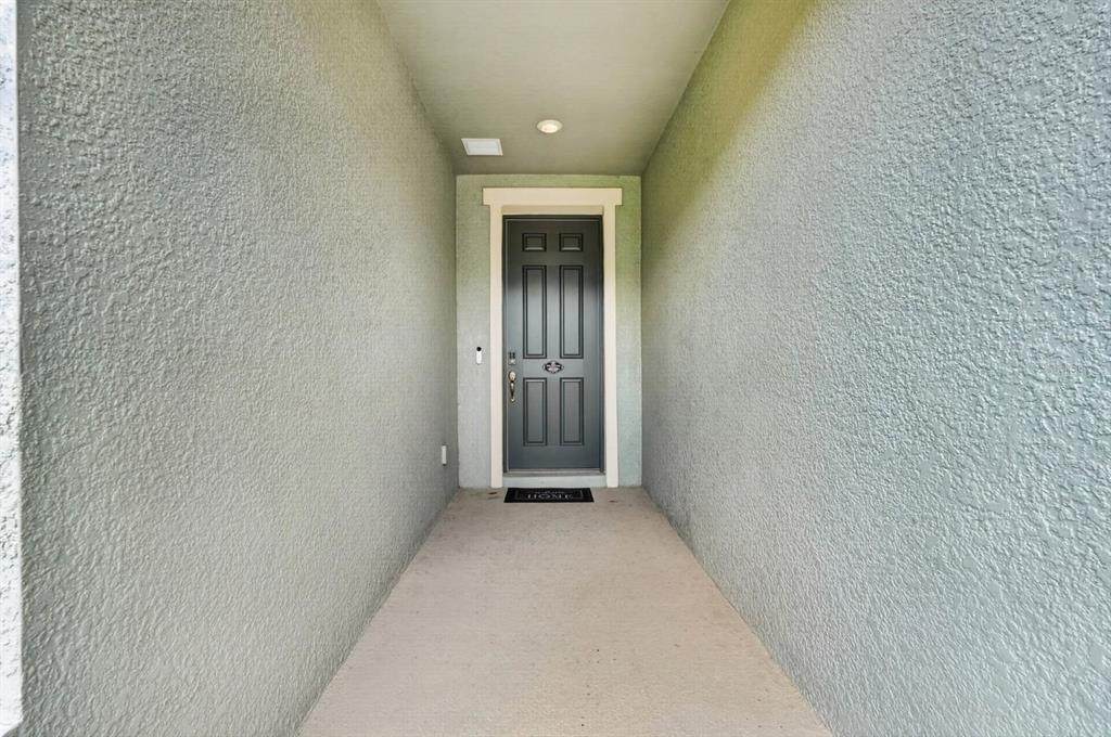 A covered entryway features a dark gray front door with glass panels and textured walls — 1196 PEARL TREE ROAD, DELTONA, FL
