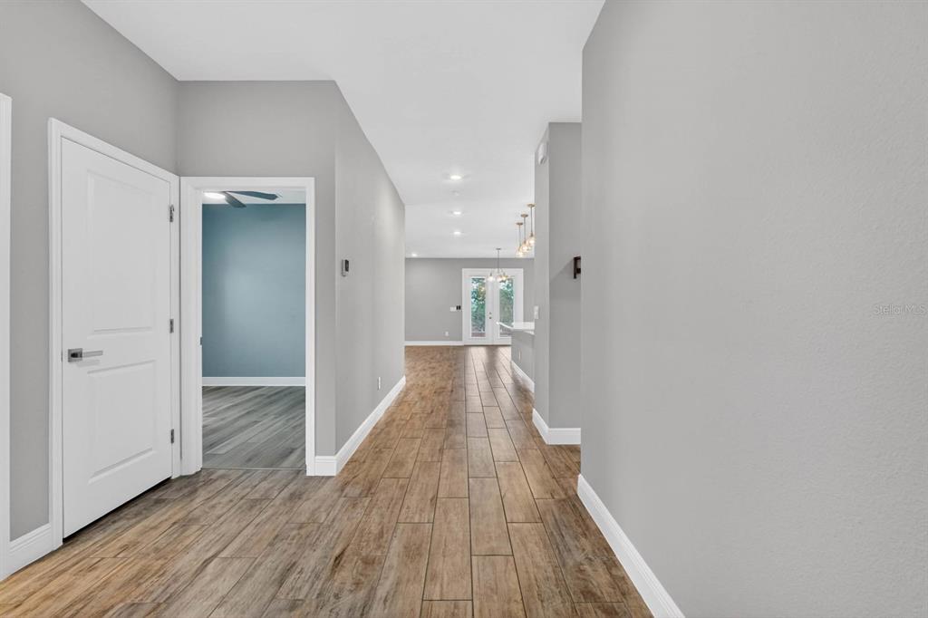A hallway with wood-look tile flooring leads toward a bright open living area — 1196 PEARL TREE ROAD, DELTONA, FL
