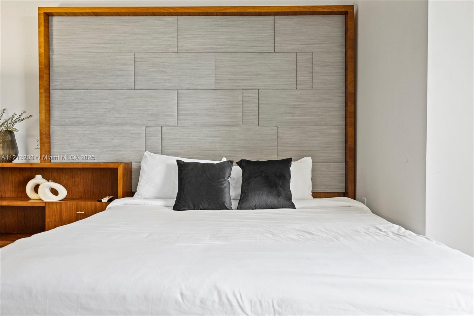 A bedroom features a large bed with a textured gray headboard and wood frame — 50 Biscayne Blvd # 605, Miami FL 33132, MIAMI, FL