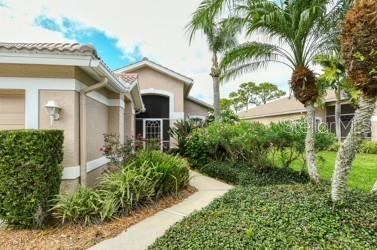 A tan stucco house exterior features a walkway, palm trees, and manicured landscaping — 9480 FOREST HILLS CIRCLE, SARASOTA, FL