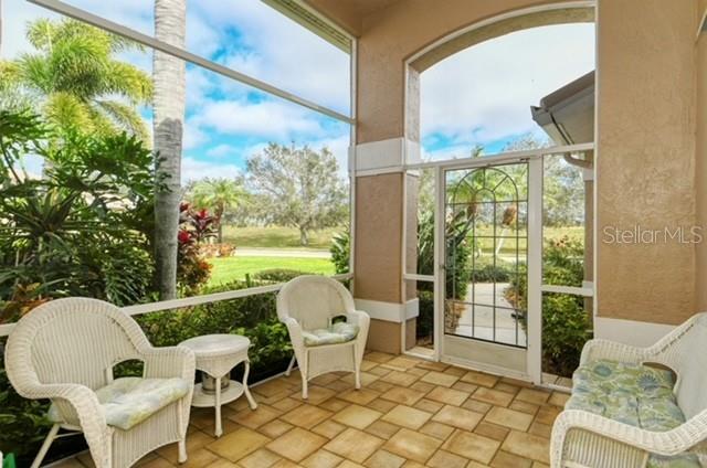 A screened-in patio features wicker furniture, tiled flooring, and a view of a grassy yard — 9480 FOREST HILLS CIRCLE, SARASOTA, FL