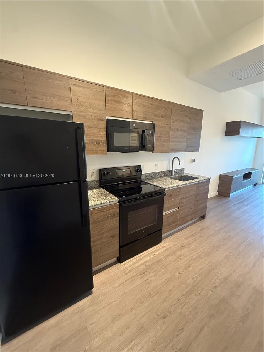 A kitchen features wood-grain cabinets, black appliances, and granite countertops in an open-concept space — 61 NW 37th Ave # 22, Miami FL 33125, MIAMI, FL