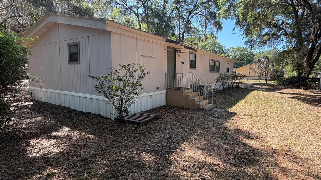 A single-story mobile home with light-colored siding, a metal staircase, and surrounding trees — 7526 NE 221ST STREET, MELROSE, FL