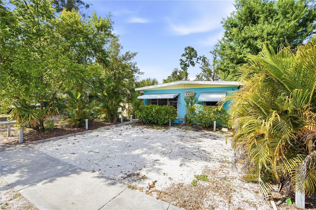 A bright blue single-story house features a gravel driveway and lush surrounding trees — 4933 13TH AVENUE S, GULFPORT, FL