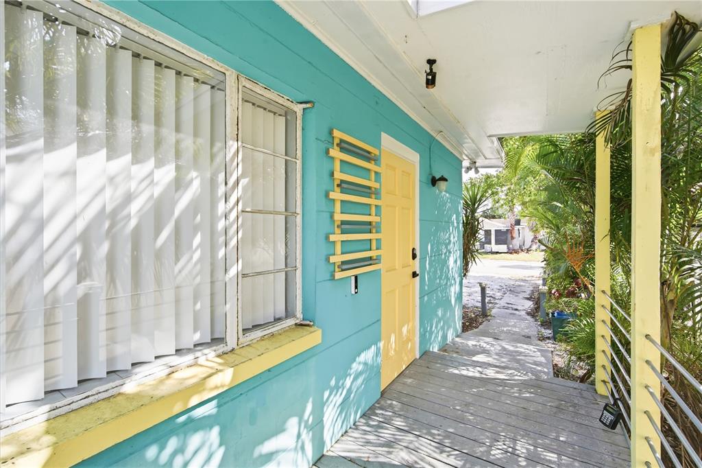 A turquoise exterior wall with a yellow door and a wooden porch under a roof — 4933 13TH AVENUE S, GULFPORT, FL