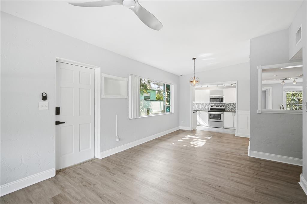 A bright living room with light wood-look flooring, a ceiling fan, and an adjacent kitchen — 4933 13TH AVENUE S, GULFPORT, FL