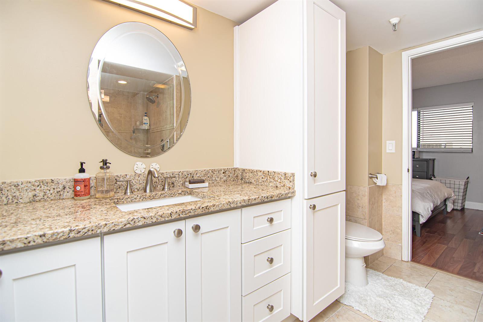 A bathroom features a granite vanity, white cabinets, a round mirror, and a toilet — 2202 S Cypress Bend Drive # 706, Pompano Beach FL 33069, POMPANO BEACH, FL