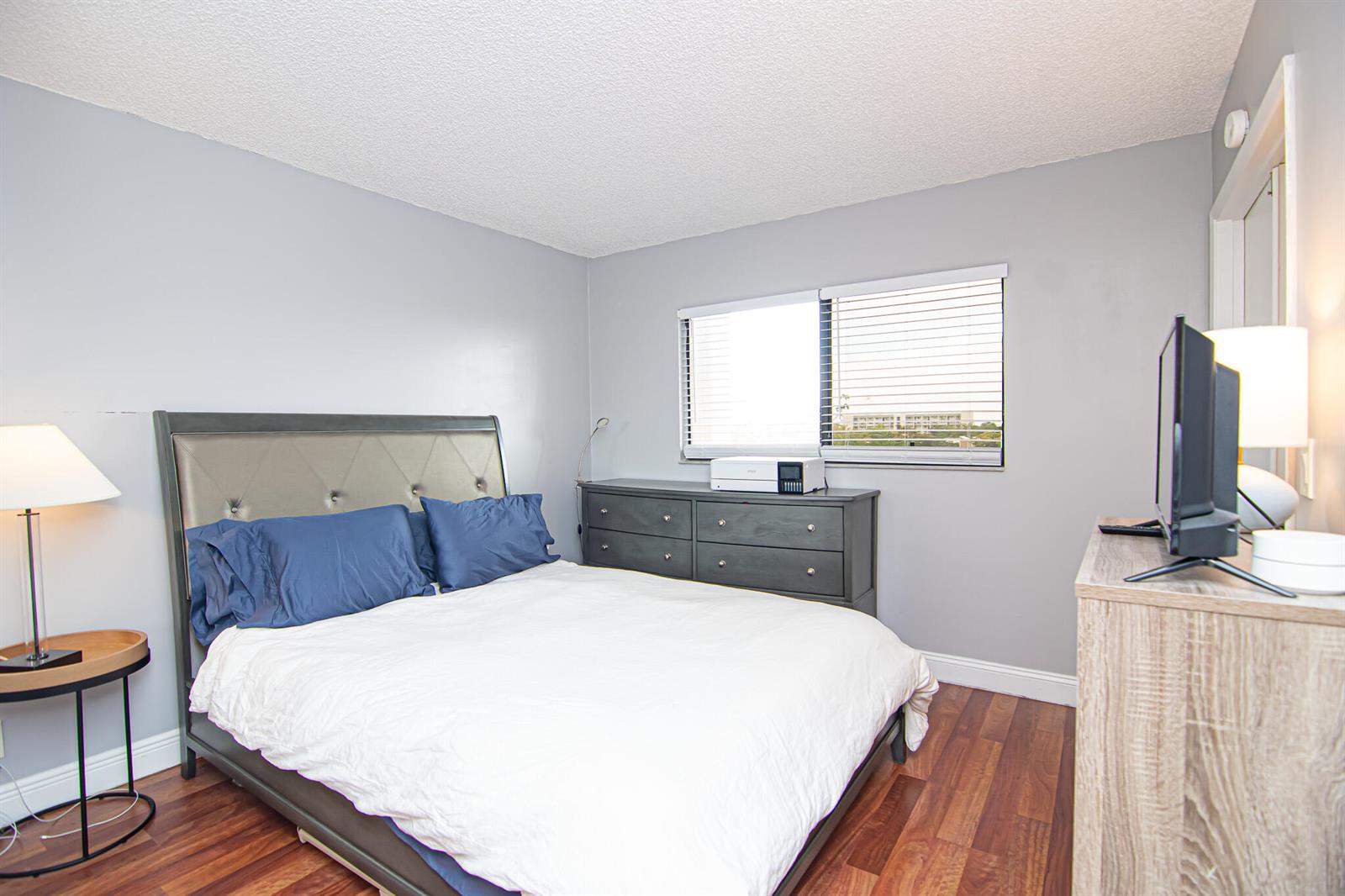 A bedroom features a bed with blue pillows, a dark dresser, and wood-look flooring — 2202 S Cypress Bend Drive # 706, Pompano Beach FL 33069, POMPANO BEACH, FL