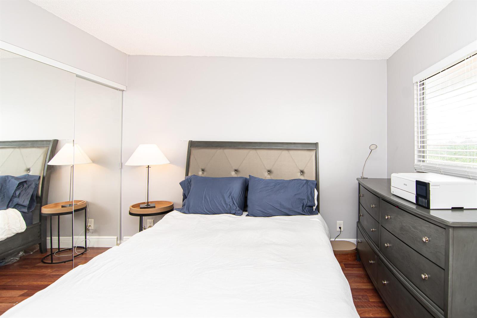 A bedroom features a bed with blue pillows, a dark dresser, and mirrored closet doors — 2202 S Cypress Bend Drive # 706, Pompano Beach FL 33069, POMPANO BEACH, FL