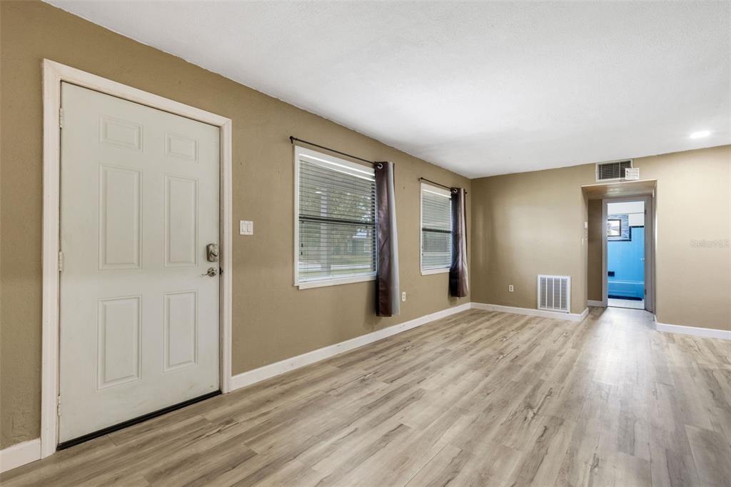An empty room with light wood-look flooring, tan walls, two windows, and a white door — 3341 CROTON TERRACE, PORT CHARLOTTE, FL