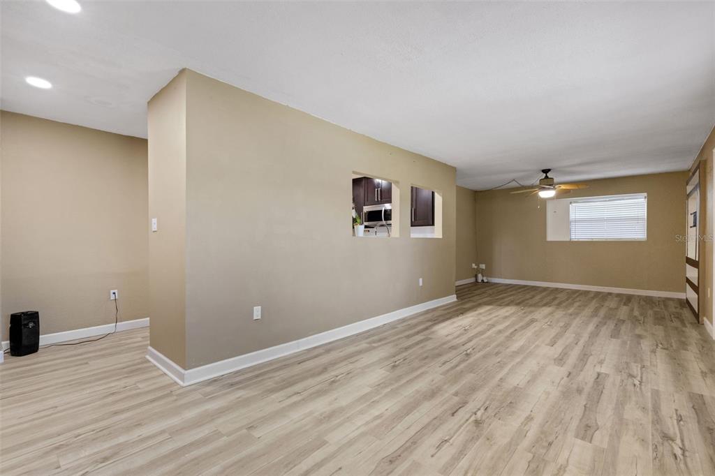 A living room with light wood-look flooring, beige walls, and a kitchen pass-through window — 3341 CROTON TERRACE, PORT CHARLOTTE, FL