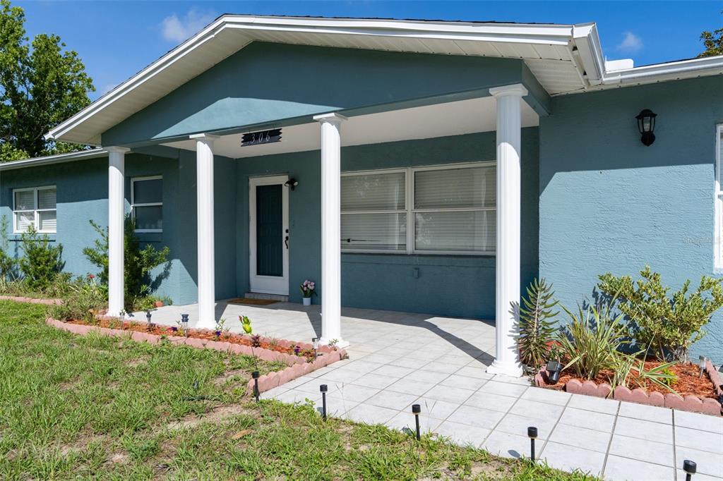 A blue house exterior features a covered front porch with white columns and tiled flooring — 306 S MONROE STREET, BEVERLY HILLS, FL