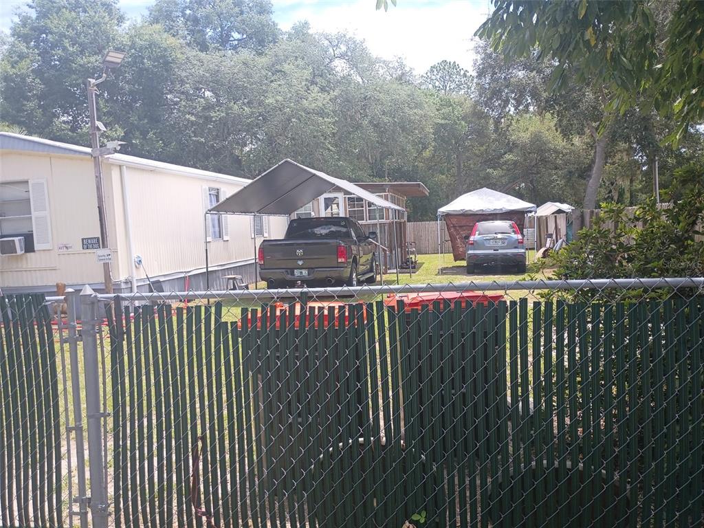 A mobile home with a metal carport and two parked vehicles behind a chain-link fence — 711 SE 129TH COURT, SILVER SPRINGS, FL