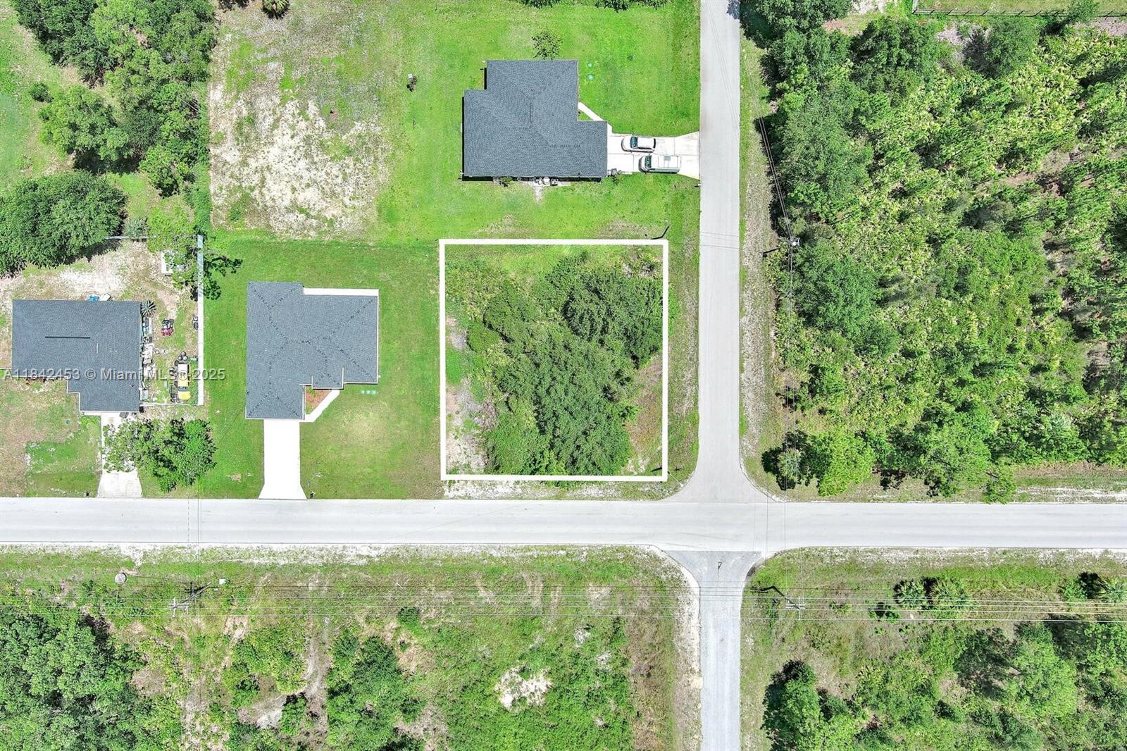 This aerial view shows a vacant, rectangular residential lot outlined in white near a road — 2500 E 10th St, Lehigh Acres FL 33936, LEHIGH ACRES, FL