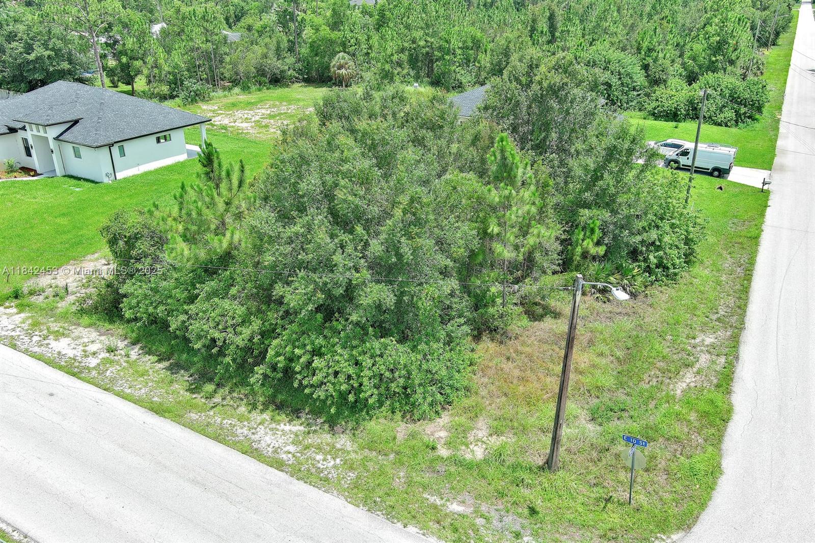 An aerial view shows a vacant, tree-covered residential lot next to a house and road — 2500 E 10th St, Lehigh Acres FL 33936, LEHIGH ACRES, FL