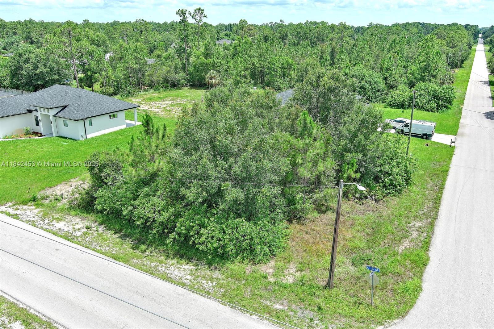 An aerial view shows a vacant, tree-covered lot situated between a house and a road — 2500 E 10th St, Lehigh Acres FL 33936, LEHIGH ACRES, FL