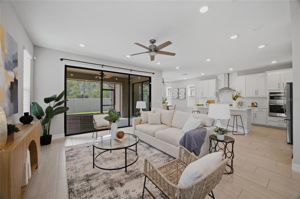 A bright open-concept living room features a white sofa, glass coffee table, and kitchen — 4667 SAN MARTINO DRIVE, WESLEY CHAPEL, FL