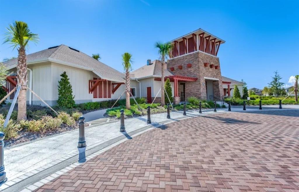 A stone and siding clubhouse exterior with a paved driveway and palm trees — 6531 TRENT CREEK DRIVE, RUSKIN, FL