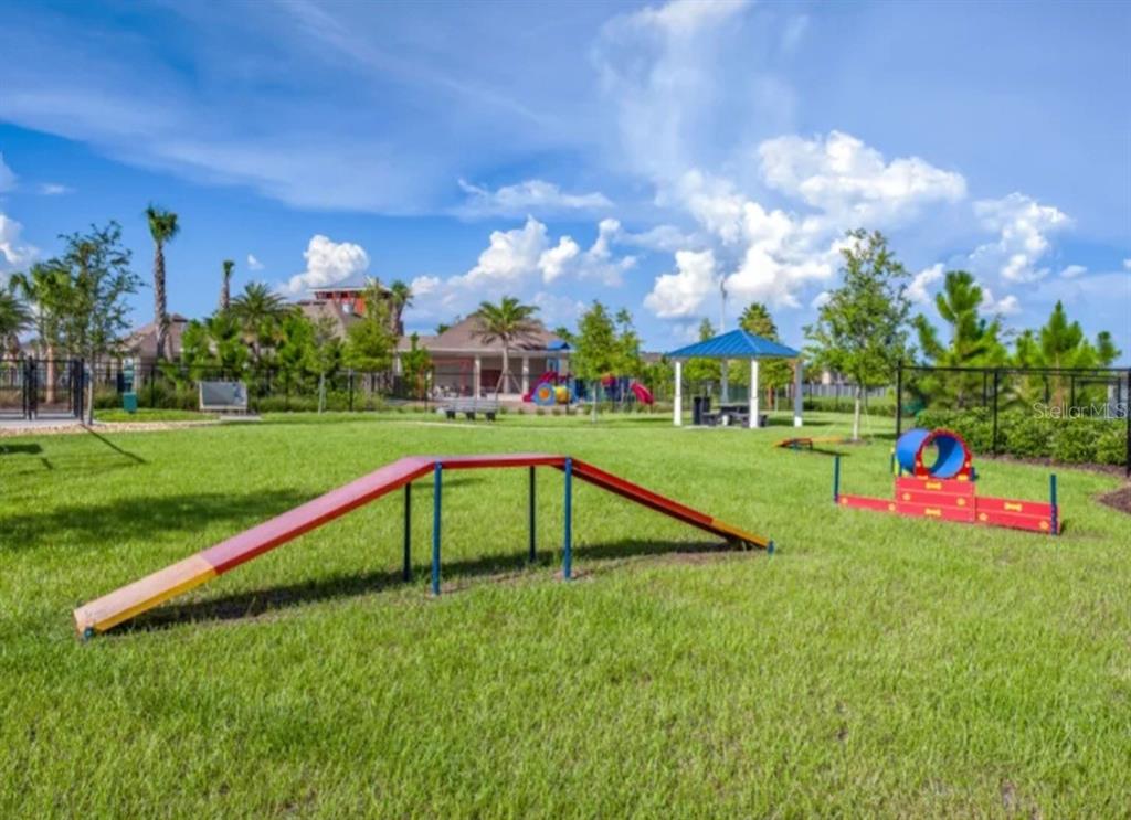 A fenced dog park features agility equipment, a blue-roofed pavilion, and surrounding trees under a sky — 6531 TRENT CREEK DRIVE, RUSKIN, FL