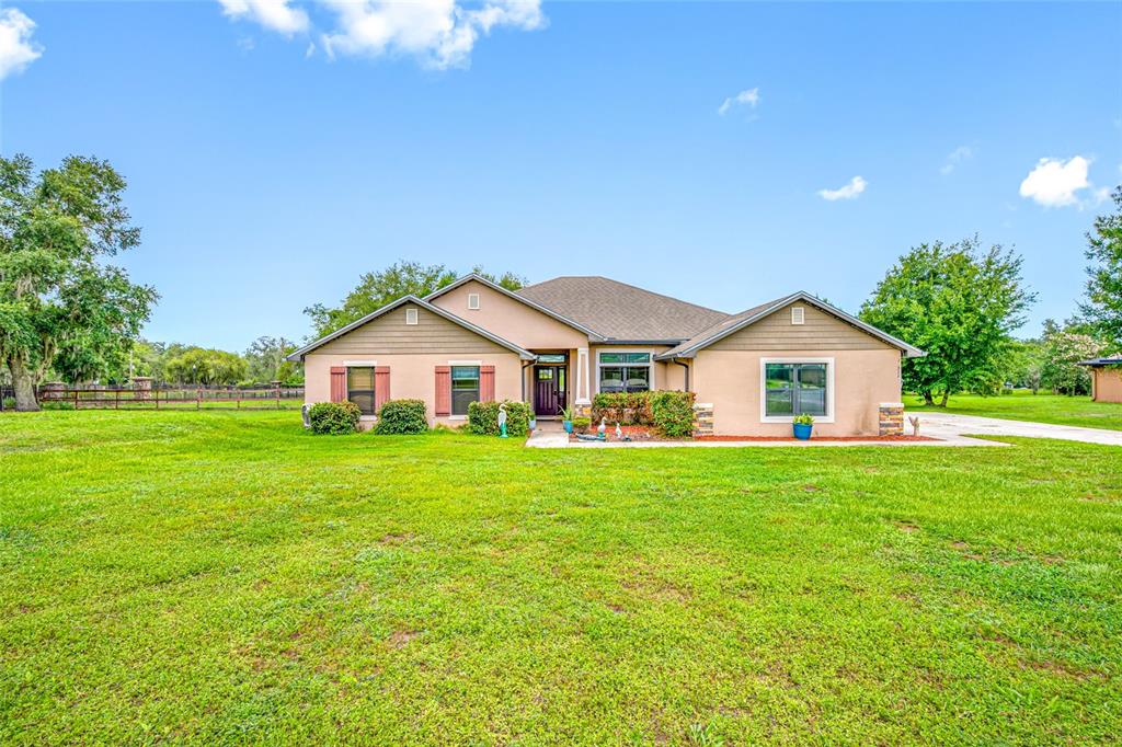 A single-story house with a tan exterior, brown roof, and a large front lawn — 14311 HILL COUNTRY LANE, DADE CITY, FL