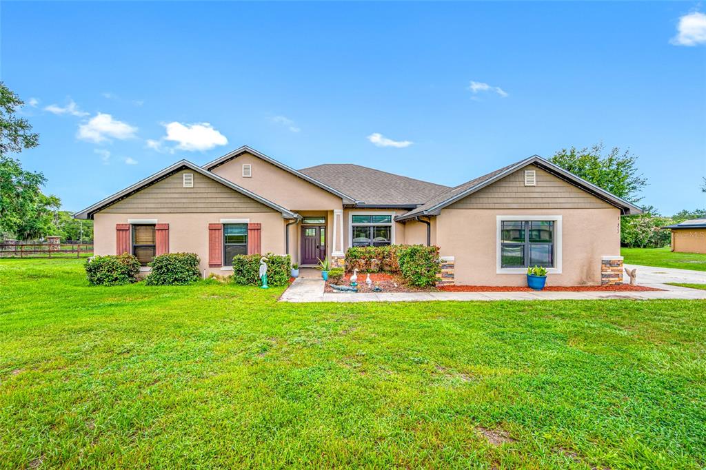 A single-story house with a tan stucco exterior, brown shingle roof, and a grassy yard — 14311 HILL COUNTRY LANE, DADE CITY, FL
