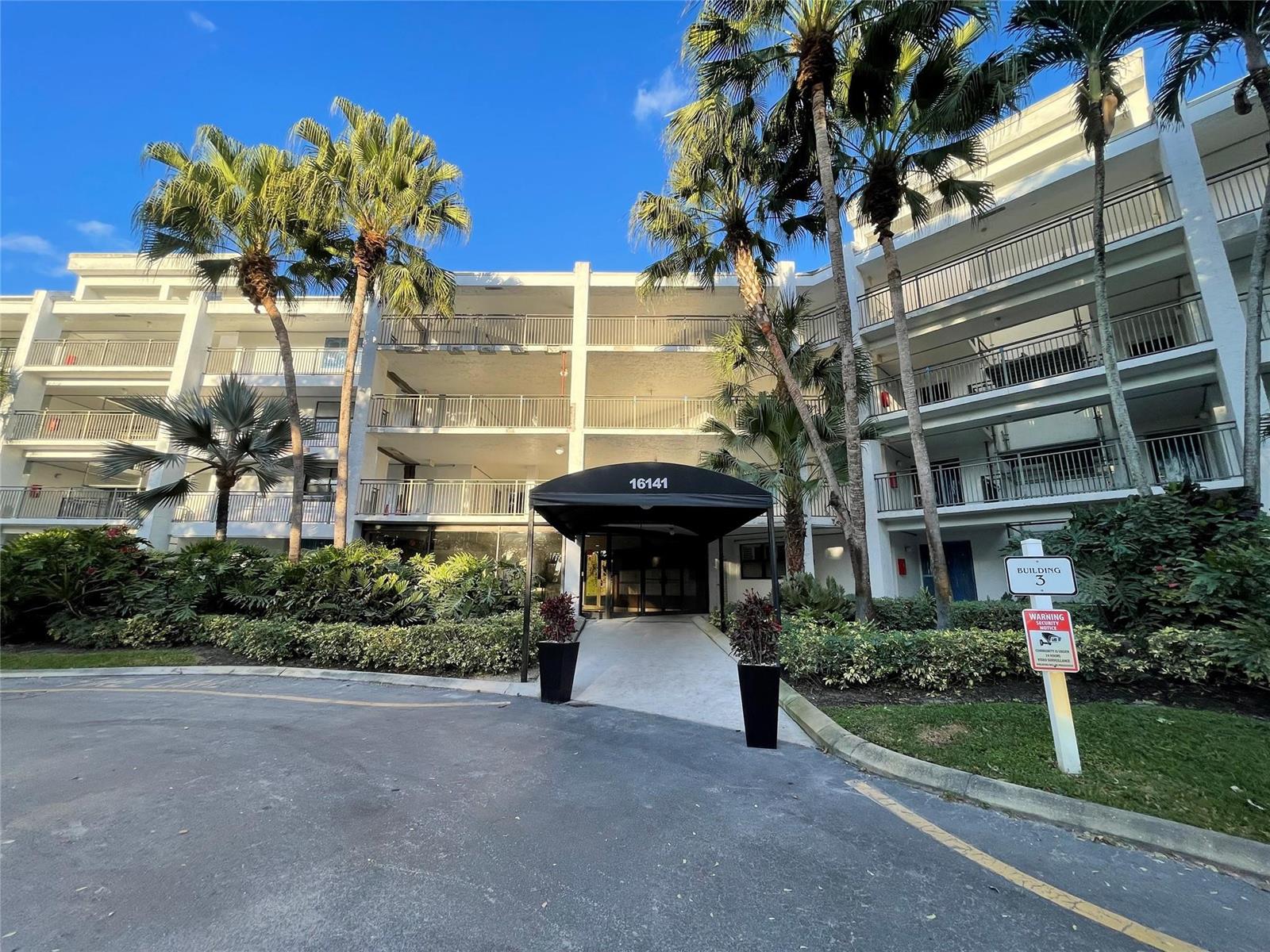 The exterior of a multi-story residential building features a covered entrance and palm trees — 16141 Blatt Boulevard # 408, Weston FL 33326, WESTON, FL