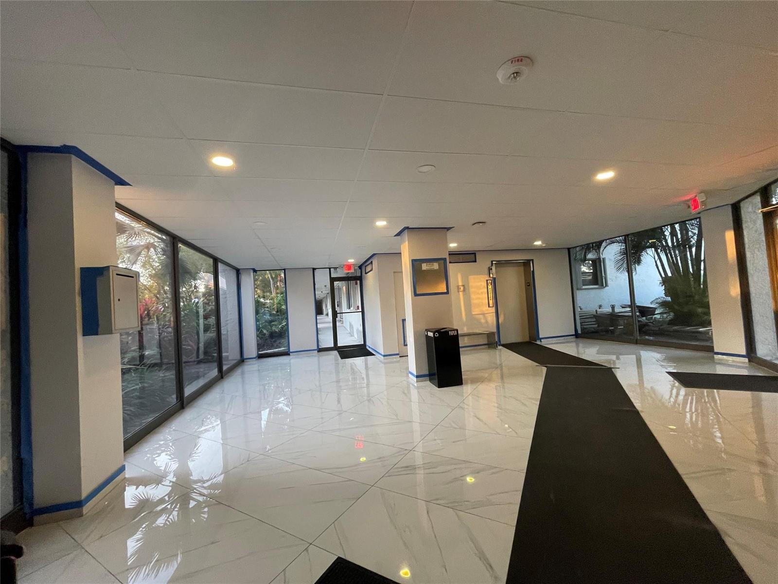 A bright lobby features white marble-look tile flooring, floor-to-ceiling windows, and an elevator — 16141 Blatt Boulevard # 408, Weston FL 33326, WESTON, FL