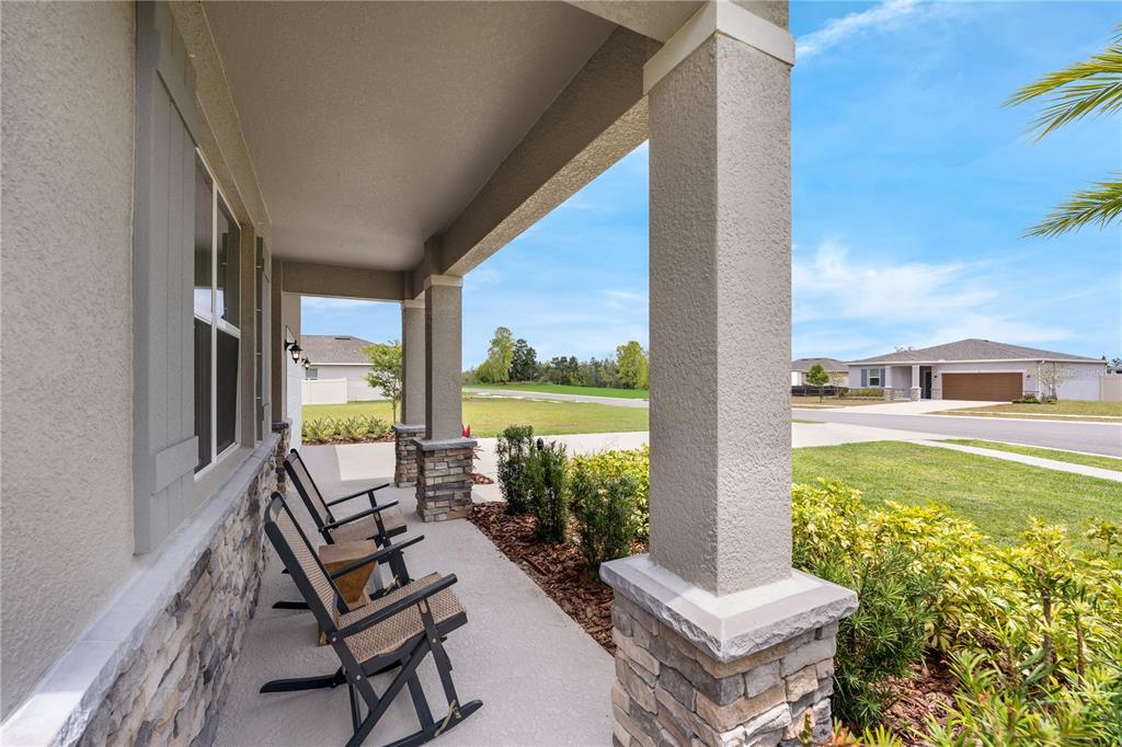 A covered front porch features stone-based columns, two rocking chairs, and a view of neighborhood homes — 1713 FLAG STREET, HAINES CITY, FL