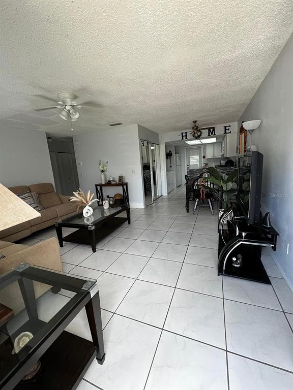 A living room with light tile flooring, a beige sofa, and a glass coffee table — 26 LAS PALMAS WAY UNIT 1, KISSIMMEE, FL
