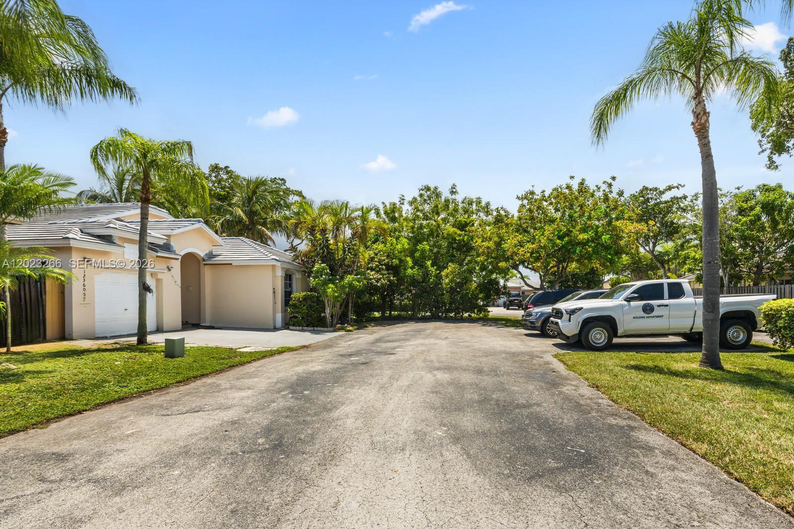 A paved driveway leads to a single-story house with a garage and parked vehicles — 12360 SW 145th St, Miami FL 33186, MIAMI, FL