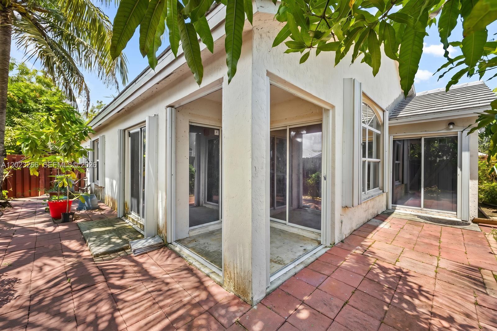A patio with red pavers sits outside a house with multiple sliding glass doors — 12360 SW 145th St, Miami FL 33186, MIAMI, FL