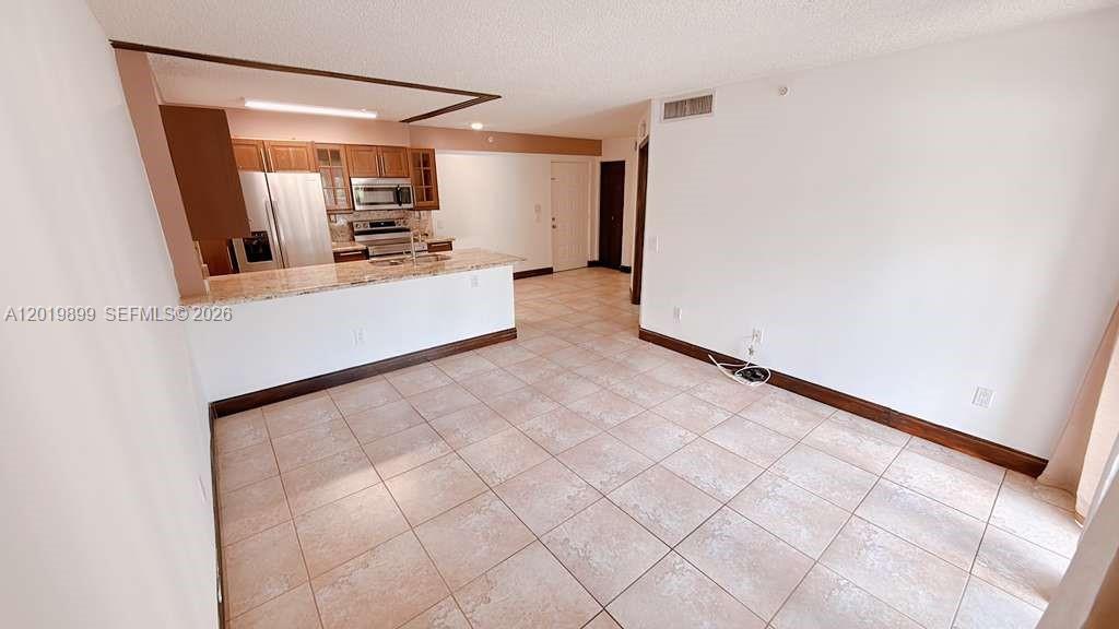 A kitchen with wood cabinets and a granite countertop overlooks an open tiled room — 470 S Park Rd # 104, Hollywood FL 33021, HOLLYWOOD, FL