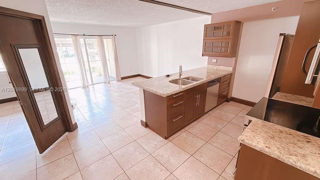 A kitchen with brown cabinets and granite countertops overlooks a tiled living area — 470 S Park Rd # 104, Hollywood FL 33021, HOLLYWOOD, FL