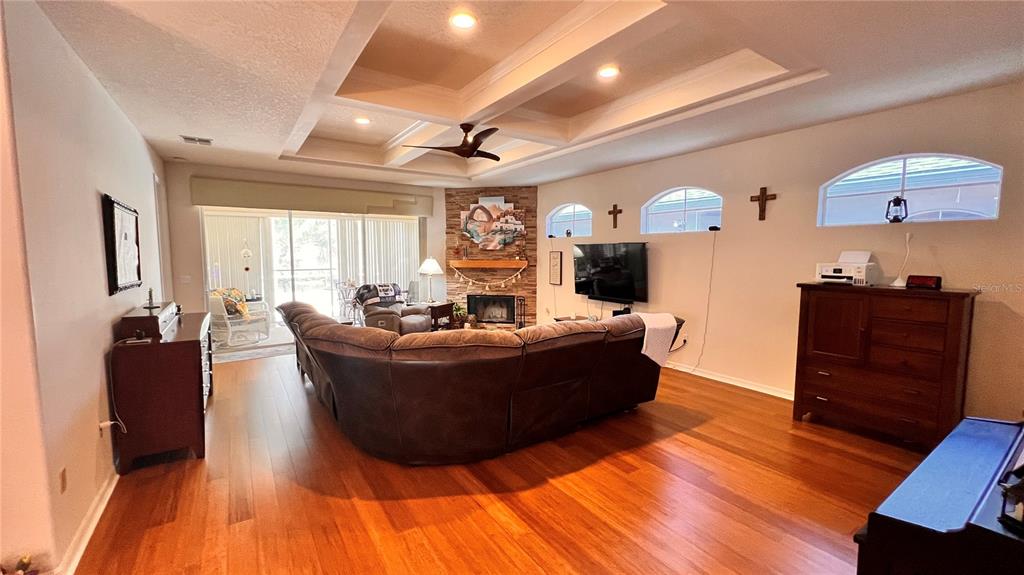 A living room features hardwood floors, a tray ceiling, a stone fireplace, and a sectional sofa — 5561 LEGEND HILLS LANE, SPRING HILL, FL
