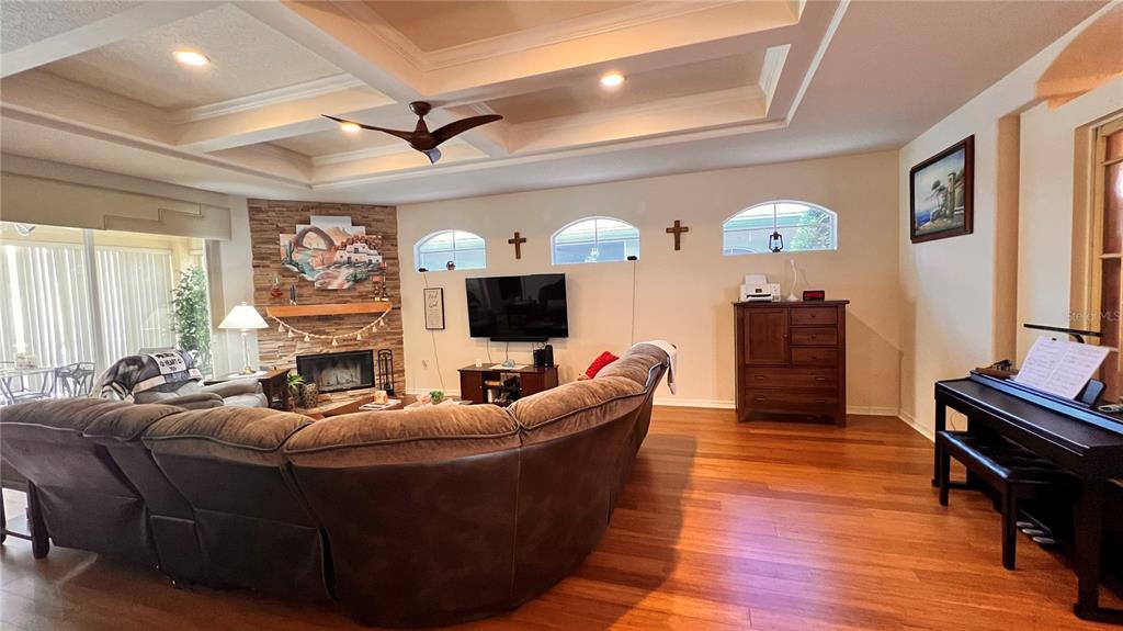 A living room features a tray ceiling, stone fireplace, hardwood floors, and a sectional sofa — 5561 LEGEND HILLS LANE, SPRING HILL, FL