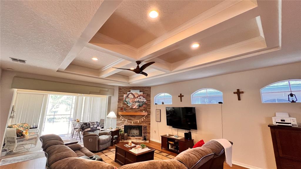 A living room features a coffered ceiling, a corner stone fireplace, and a television console — 5561 LEGEND HILLS LANE, SPRING HILL, FL