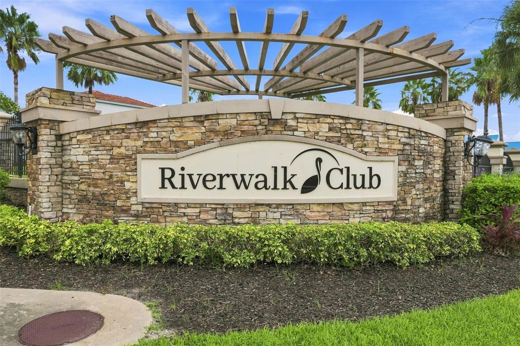 A stone monument sign for Riverwalk Club sits beneath a wooden pergola with palm trees — 1805 NOEL PLACE UNIT 101, MELBOURNE, FL