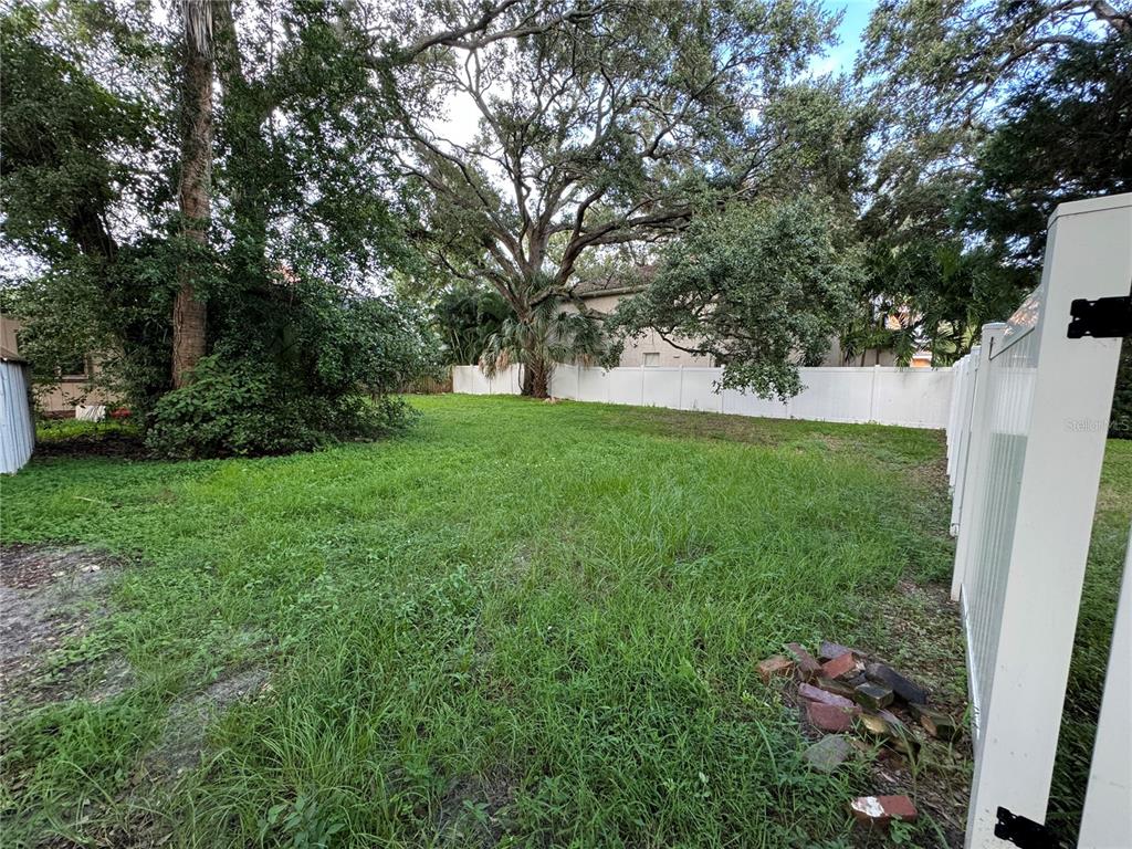 A grassy backyard features a large tree, a white vinyl fence, and scattered bricks — 3115 W SAN PEDRO STREET, TAMPA, FL