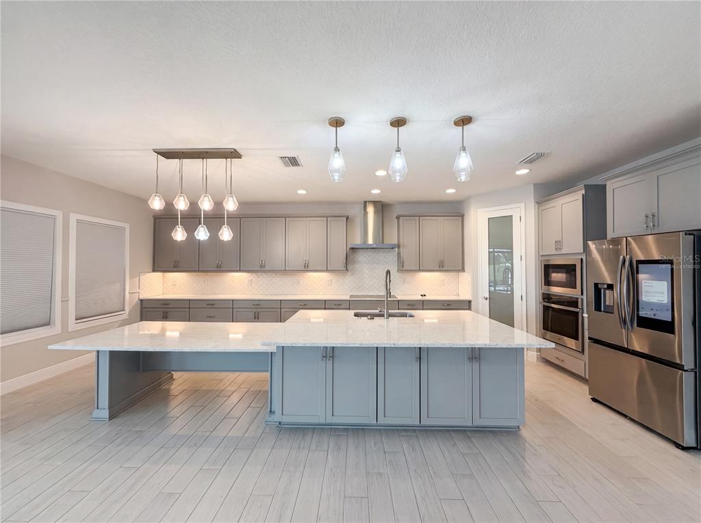 A modern kitchen features gray cabinetry, a large white quartz island, and stainless steel appliances — 13176 TWIN BRIDGES DRIVE, RIVERVIEW, FL