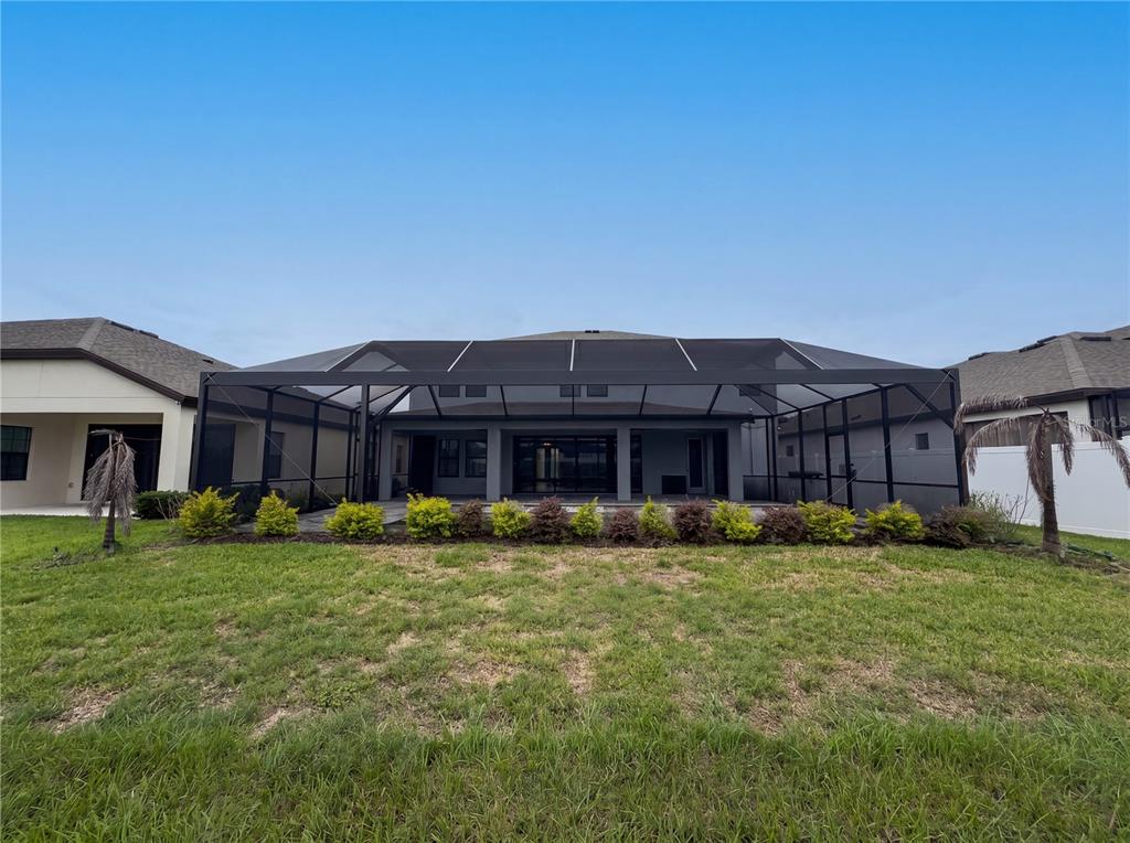 A backyard view of a house with a large screened-in lanai and landscaped garden beds — 13176 TWIN BRIDGES DRIVE, RIVERVIEW, FL