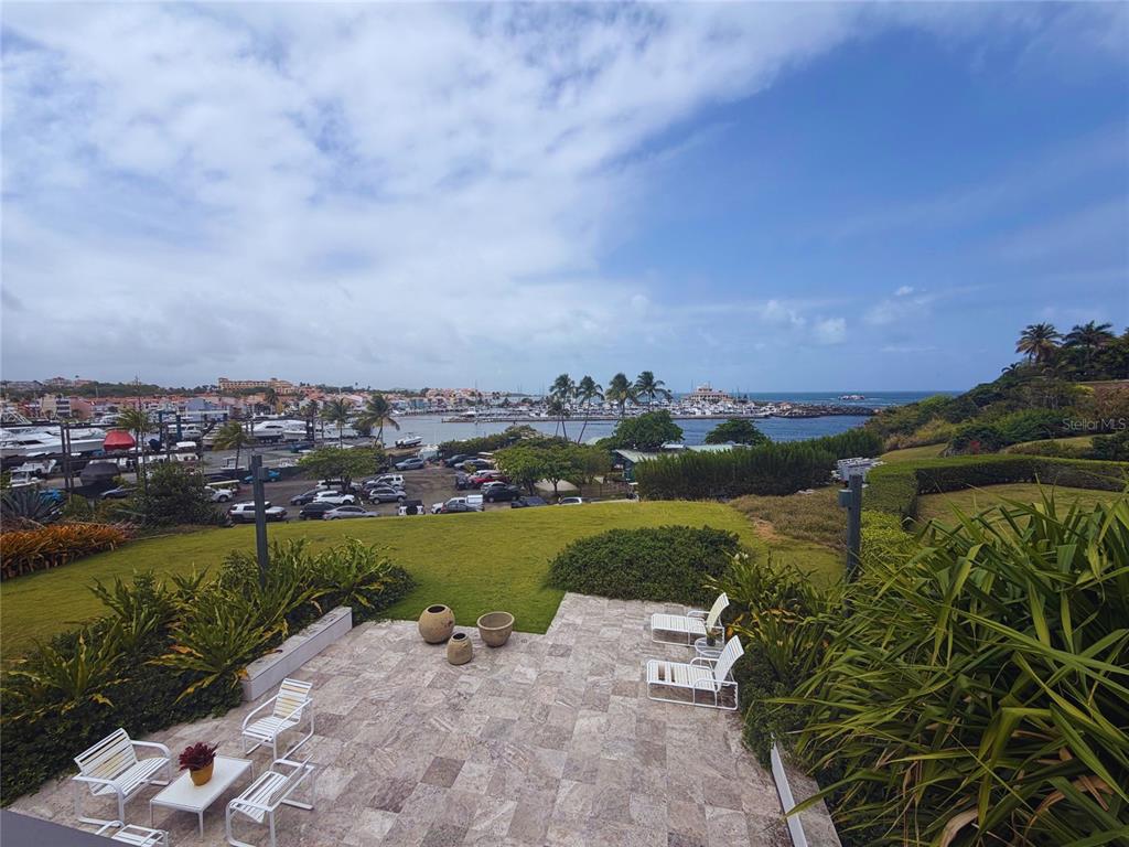 A stone patio with outdoor furniture overlooks a grassy lawn, a marina, and the ocean — 24.25 HARBORVIEW ROAD, HUMACAO, PR