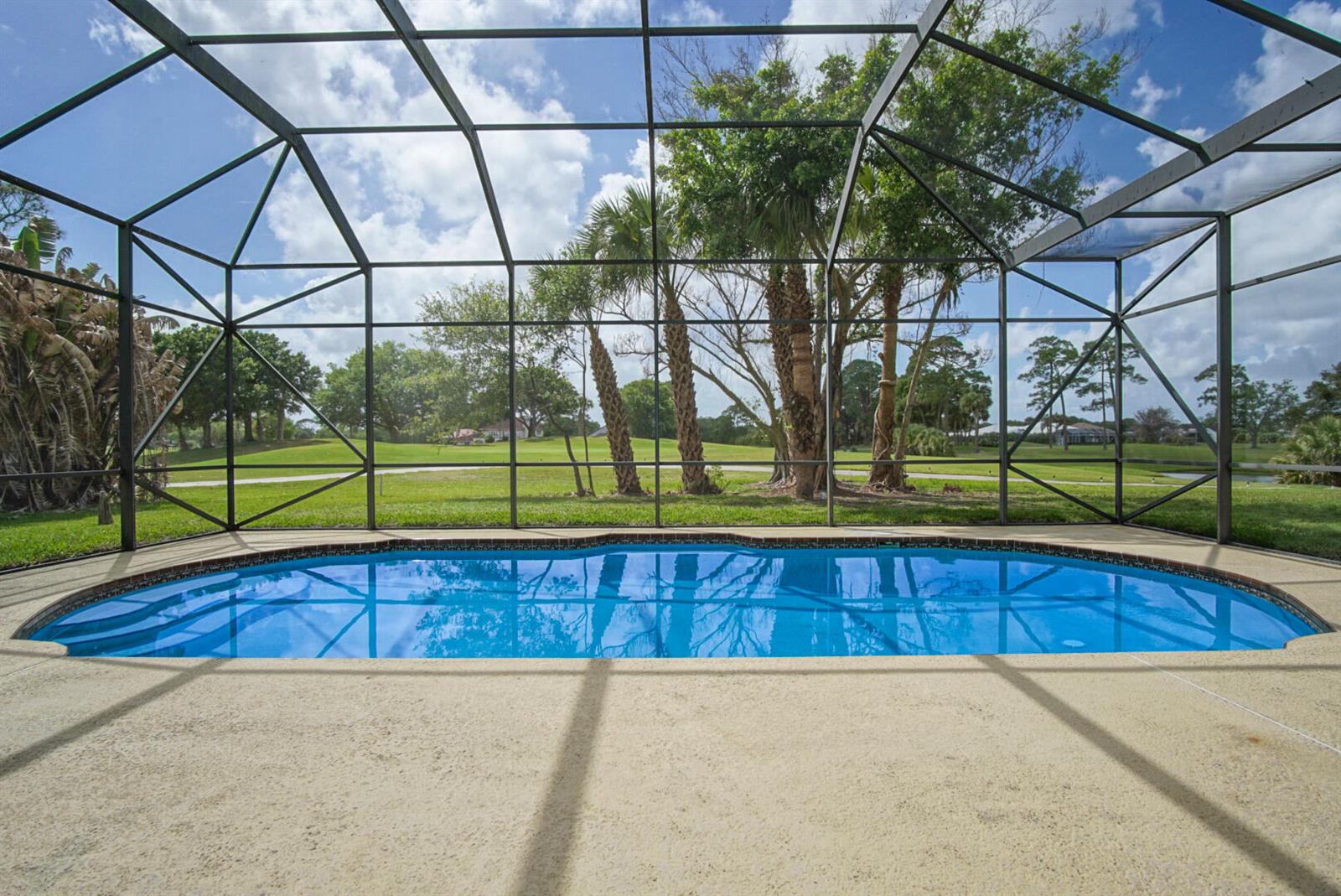 A screened-in swimming pool overlooks a grassy golf course with palm trees under a blue sky — 2987 Conifer Drive, Fort Pierce FL 34951, FORT PIERCE, FL
