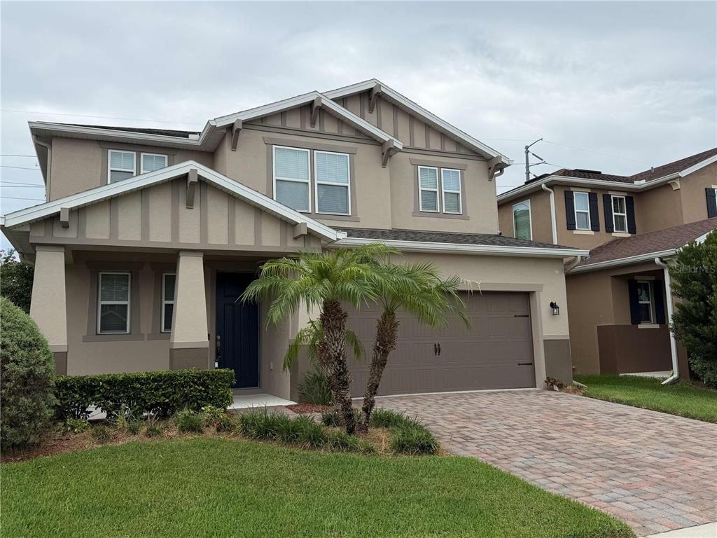 A two-story suburban house with a tan stucco exterior, a palm tree, and a paved driveway — 476 BOTTLEBRUSH LOOP, SANFORD, FL