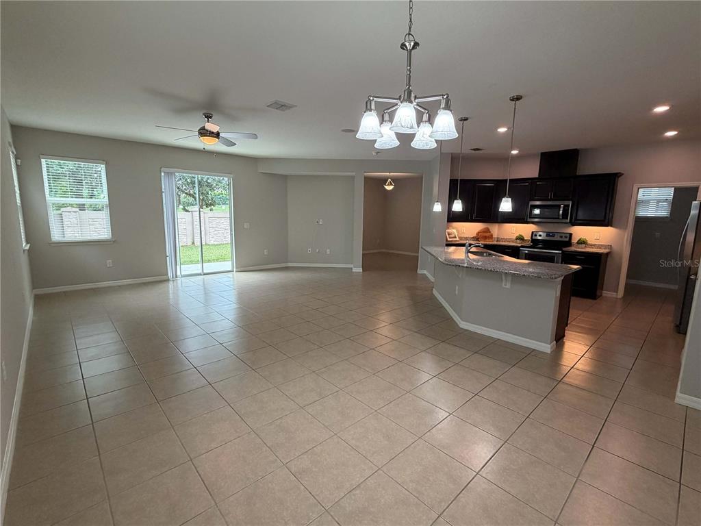 An open-concept kitchen and living area features tile flooring, dark cabinetry, and a granite island — 476 BOTTLEBRUSH LOOP, SANFORD, FL