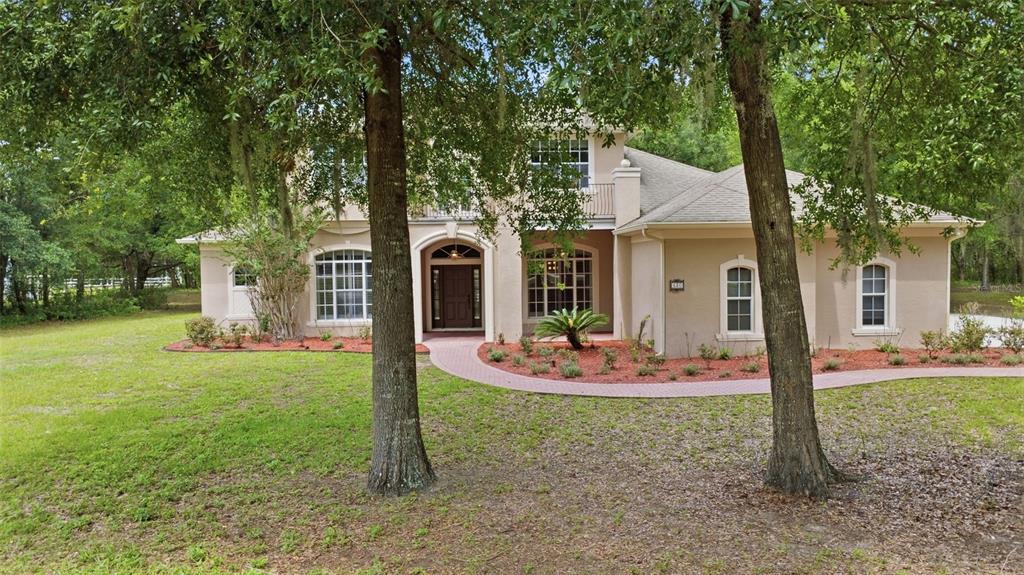 A two-story beige house with a brick walkway sits among trees on a grassy lot — 530 N BLUE LAKE AVENUE, DELAND, FL