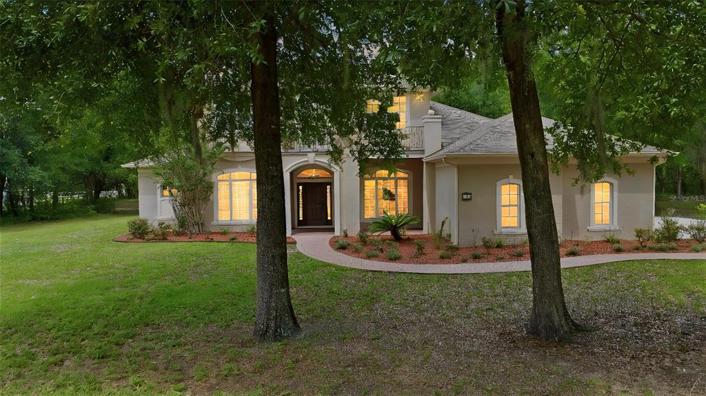 A two-story stucco house with a arched entryway sits behind two large trees — 530 N BLUE LAKE AVENUE, DELAND, FL