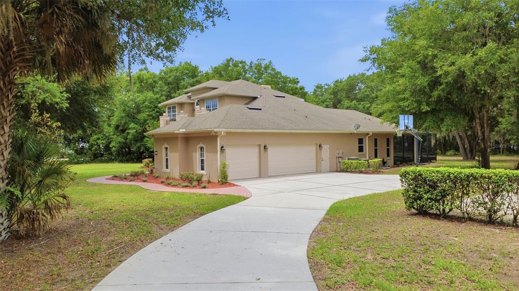 A tan two-story house with a three-car garage and a concrete driveway surrounded by trees — 530 N BLUE LAKE AVENUE, DELAND, FL